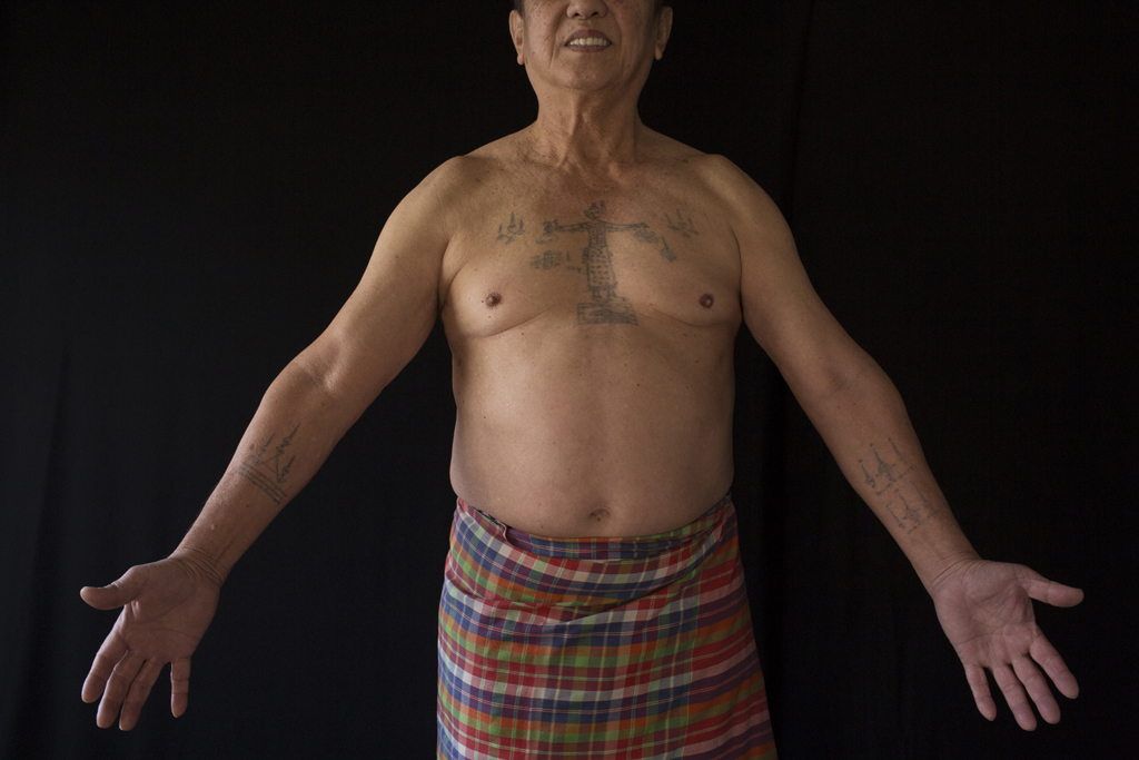 Full Image Kim Hak's photograph of a shirtless Cambodian man, with tattoos and wearing a traditional kroma