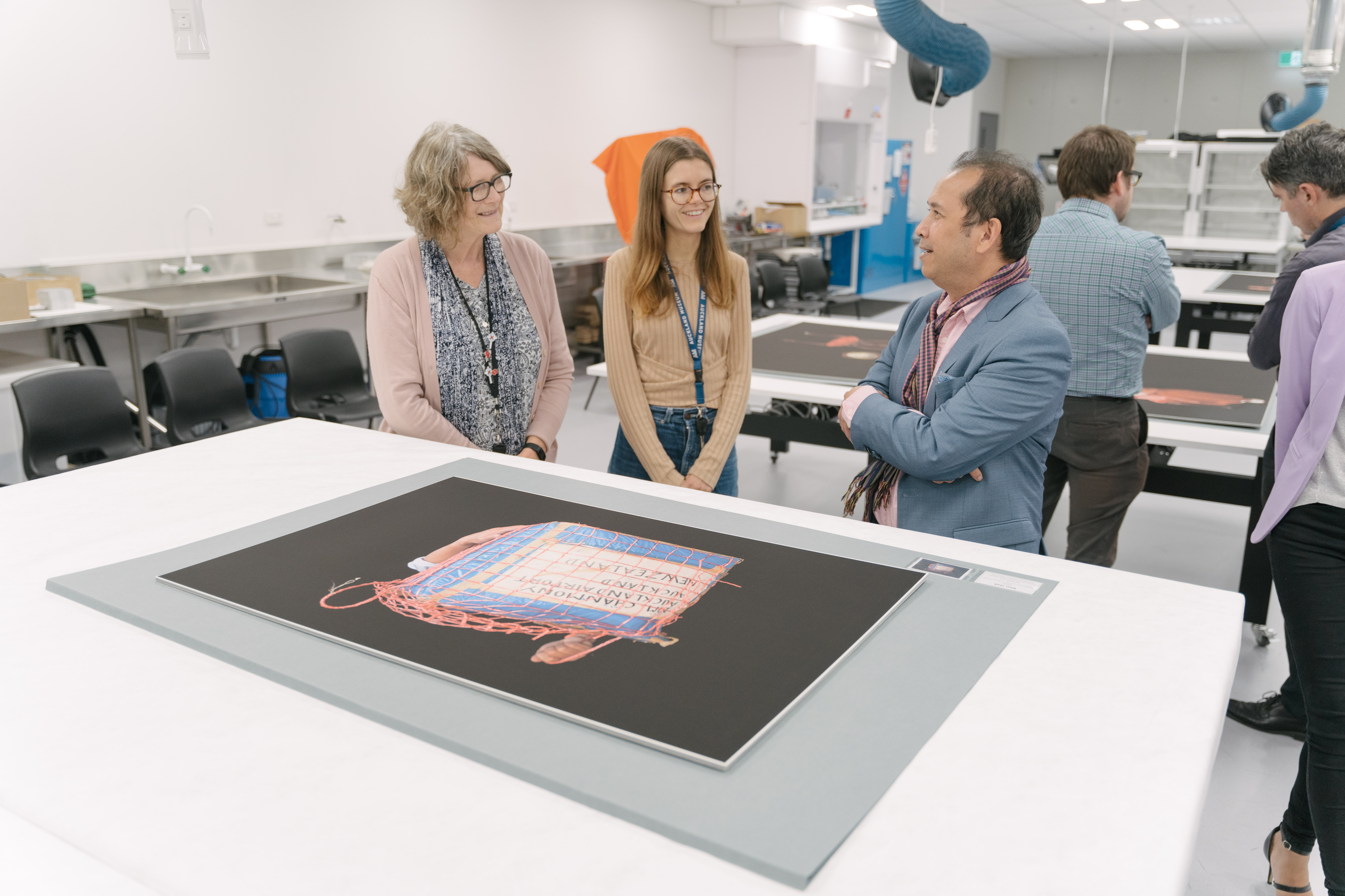 A member of the Cambodian community and two Museum staff members view Kim Hak's works containing the box in which refugees would carry their belongings