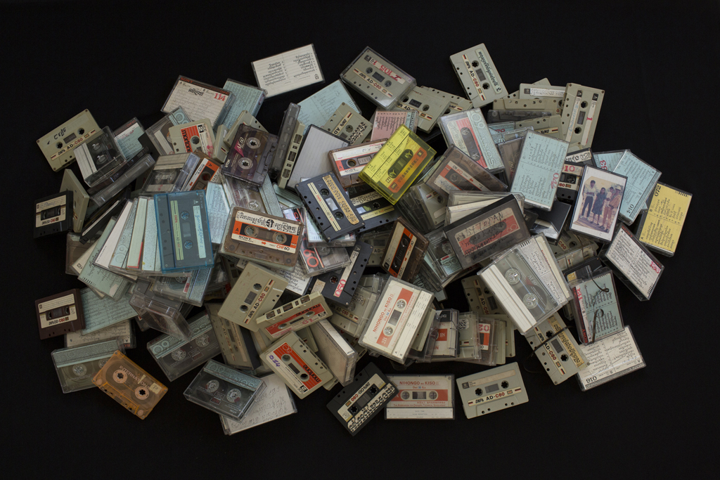 Full Image Kim Hak's photograph of a large pile of cassettes with labels in the Khmer language strewn atop one another