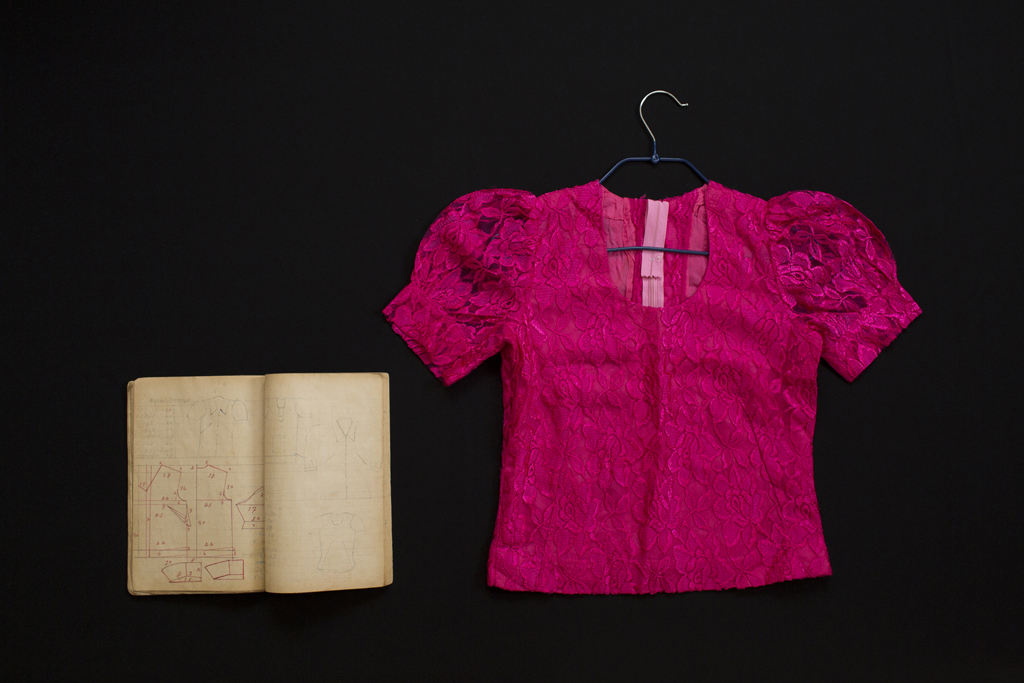 Full Image Kim Hak's photograph of a woman's pink lace top next to a book of hand-drawn sewing patterns