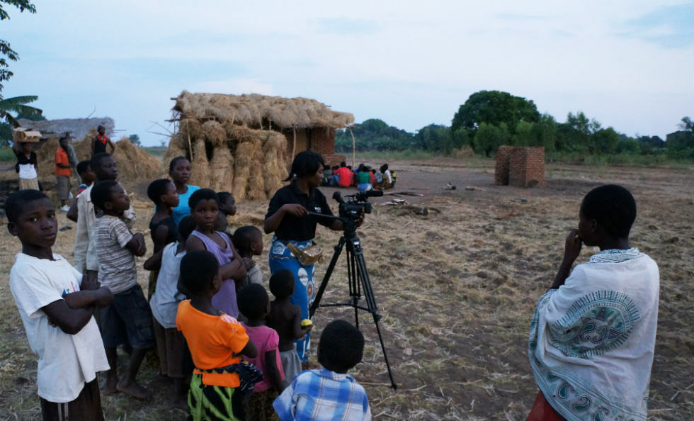 Slider Image Member of the technical team, Chimwemwe Sumani, operating her camera with local children watching on.