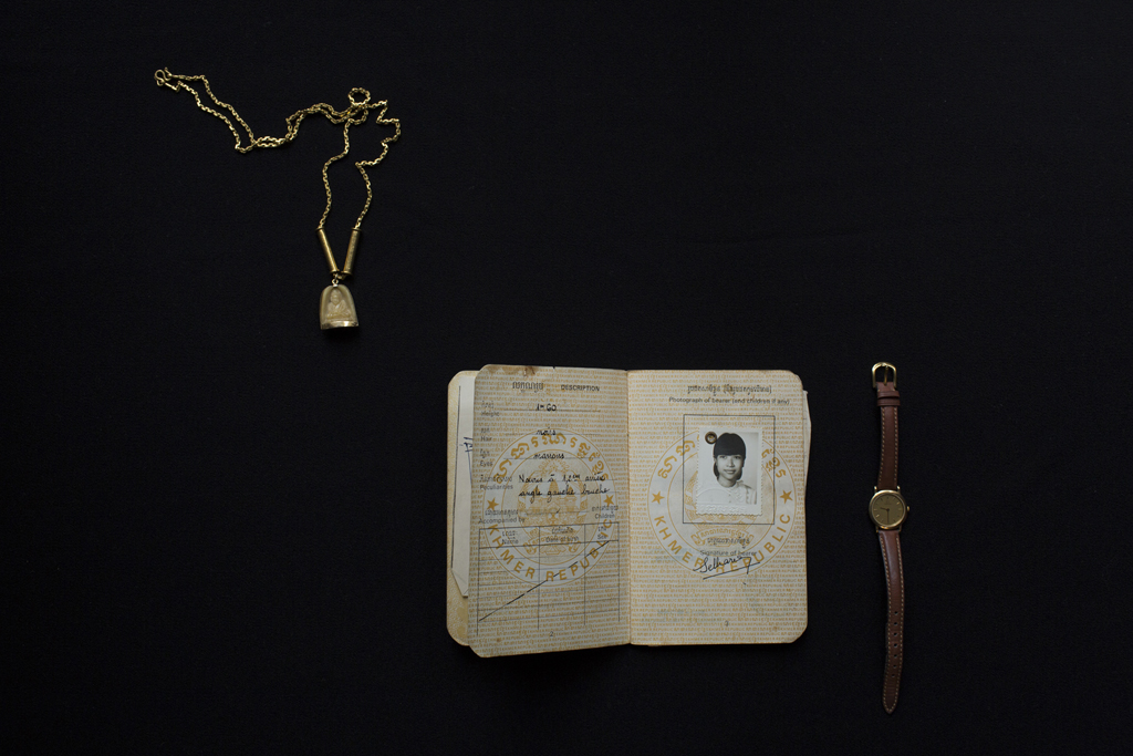 Slider Image GOLD NECKLACE WITH BUDDHA PENDANT, PASSPORT, AND WATCH. PHOTOGRAPH BY KIM HAK <br>仏様のペンダントトップがついた金のネックレス、パスポート、腕時計　写真：キム・ハク