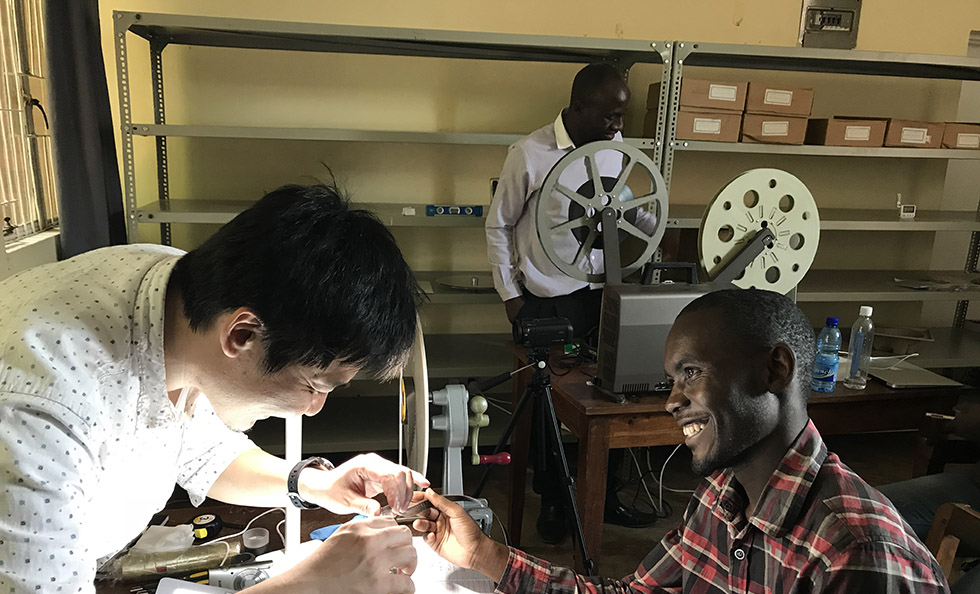 Slider Image Tokyo Koon's technical consultant Nobukazu Suzuki working with Robert Mkuwira on cleaning, repairing and digitising reel-to-reel film.